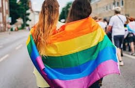 Deux femmes dans la rue portant un drapeau LGBTQIA+ et de tenant l'une contre l'autre