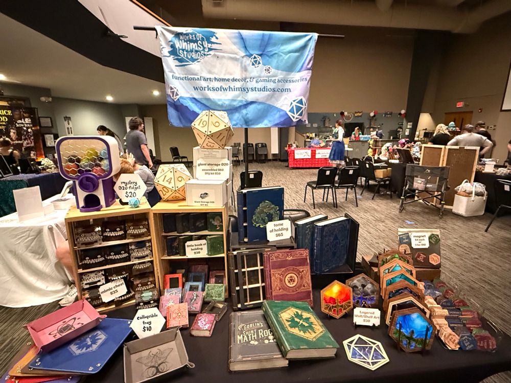 A vendor set up at a small indoor market, table filled with nerdy goodies. 