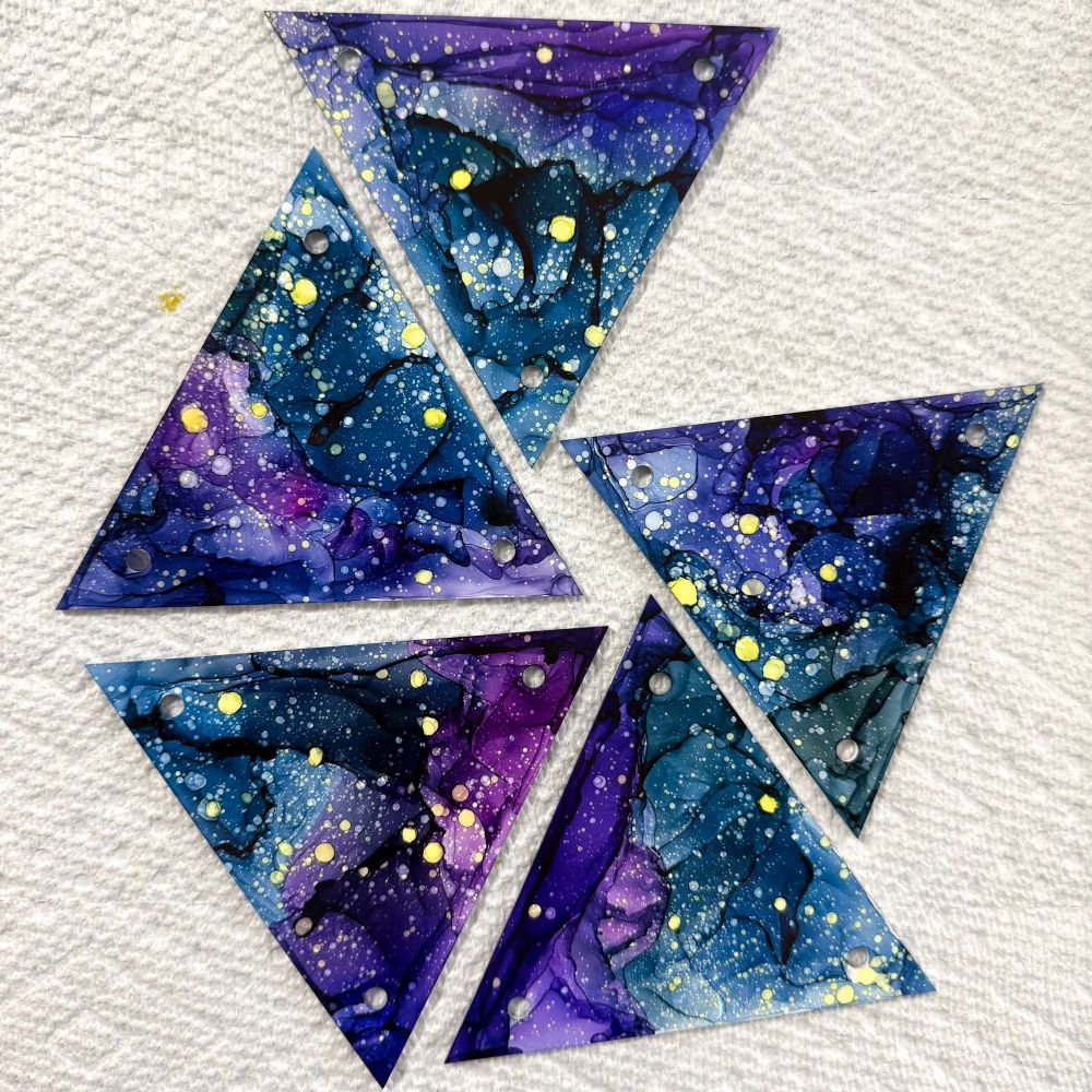 5 triangles painted with vibrant blues and purples with yellow star dots on a white background.