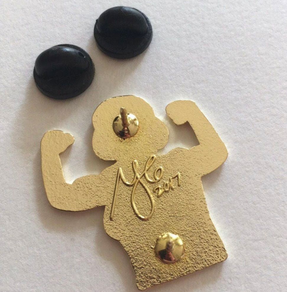 gold enamel pin with a woman flexing muscles, the words “refuse resist” on her tank top - backside of pin showing 2 posts (to keep pin from rotating) 