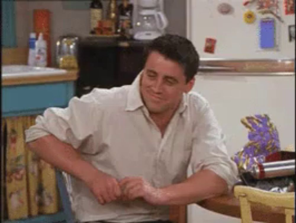 a man in a white shirt is sitting at a table in front of a fridge