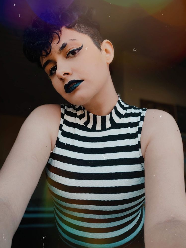 Selfie of Sunny wearing a black and white striped top, black lipstick and black winged eyeliner, looking to the camera from above.
