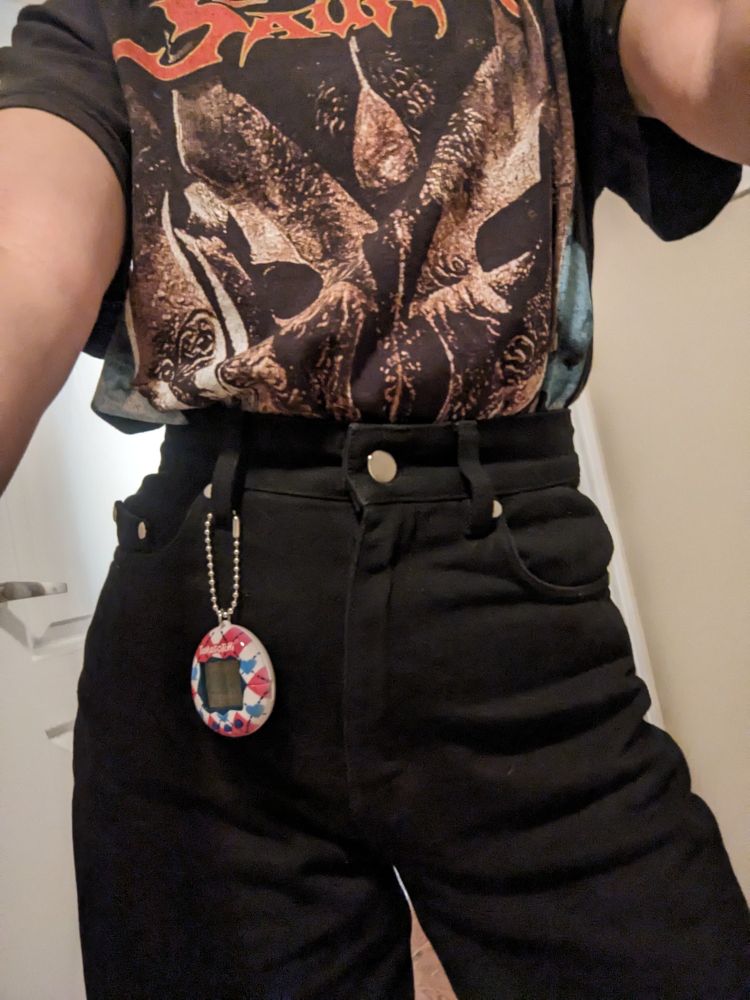 A young woman in black jeans and a Sauron t-shirt wears a Tamagotchi attached to her belt loop