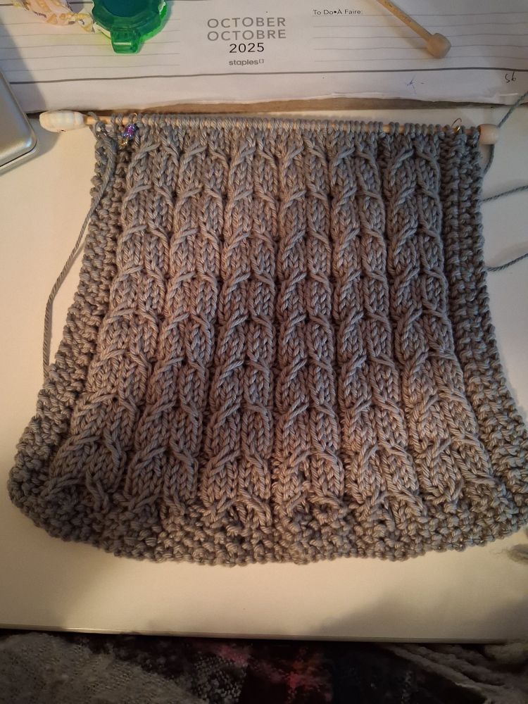 Work in progress of a hand knitted hanging towel in a smokey grey. Design shows rows with curves inside, akin to fish scales.