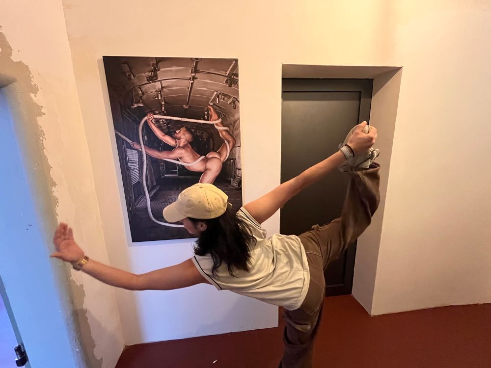 ich stehe vor einem bild in einer gefängniszelle und mache die standwaagen-pose des bildes nach 