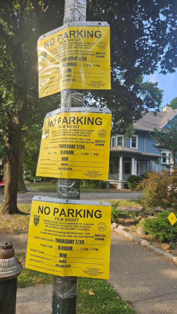 Bright yellow filming permits tacked to a pole. A light blue Victorian house in the background. The title of the production? HIM