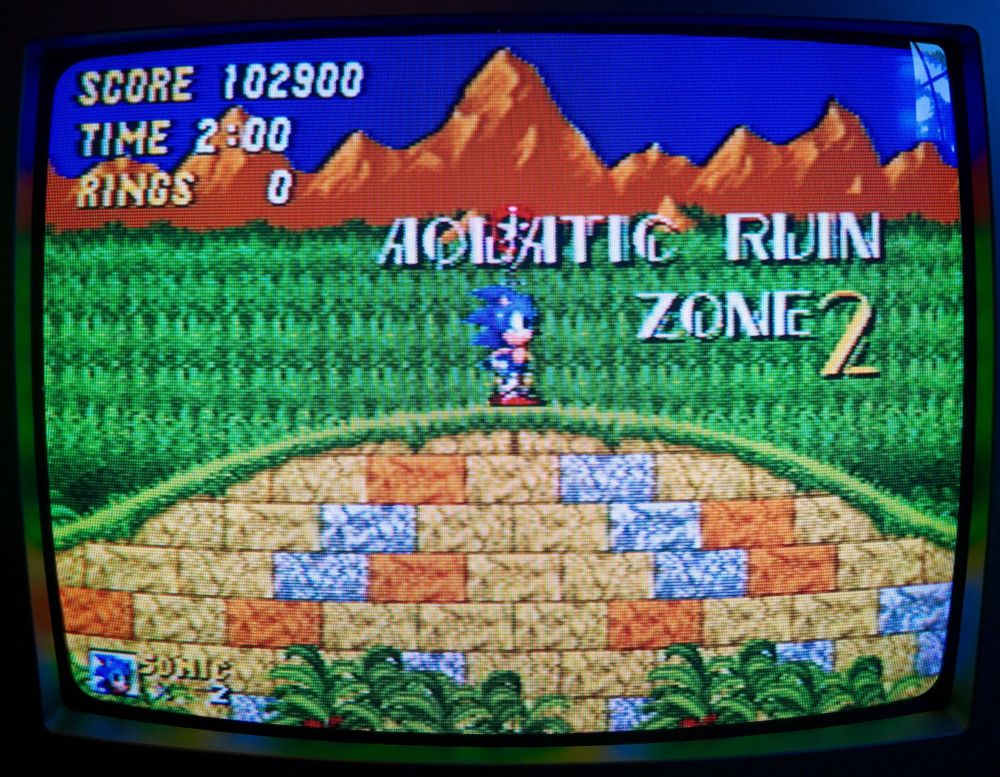 Screenshot of Sonic 2 on a CRT TV. Sonic stands on a hill at a checkpoint.