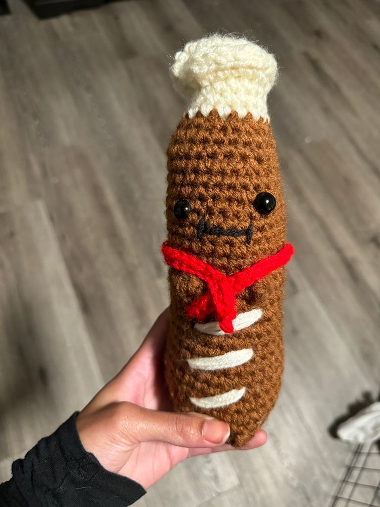 My hand holding a little crocheted baguette with a white chef's hat and a red scarf. 

His name is Beau. Beau the Baguette. 