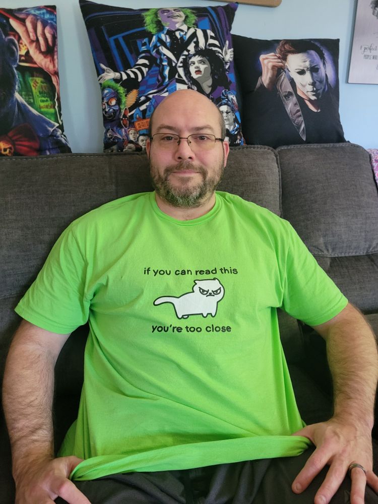 A handsome man in a neon green tee that has a white cat and saying 