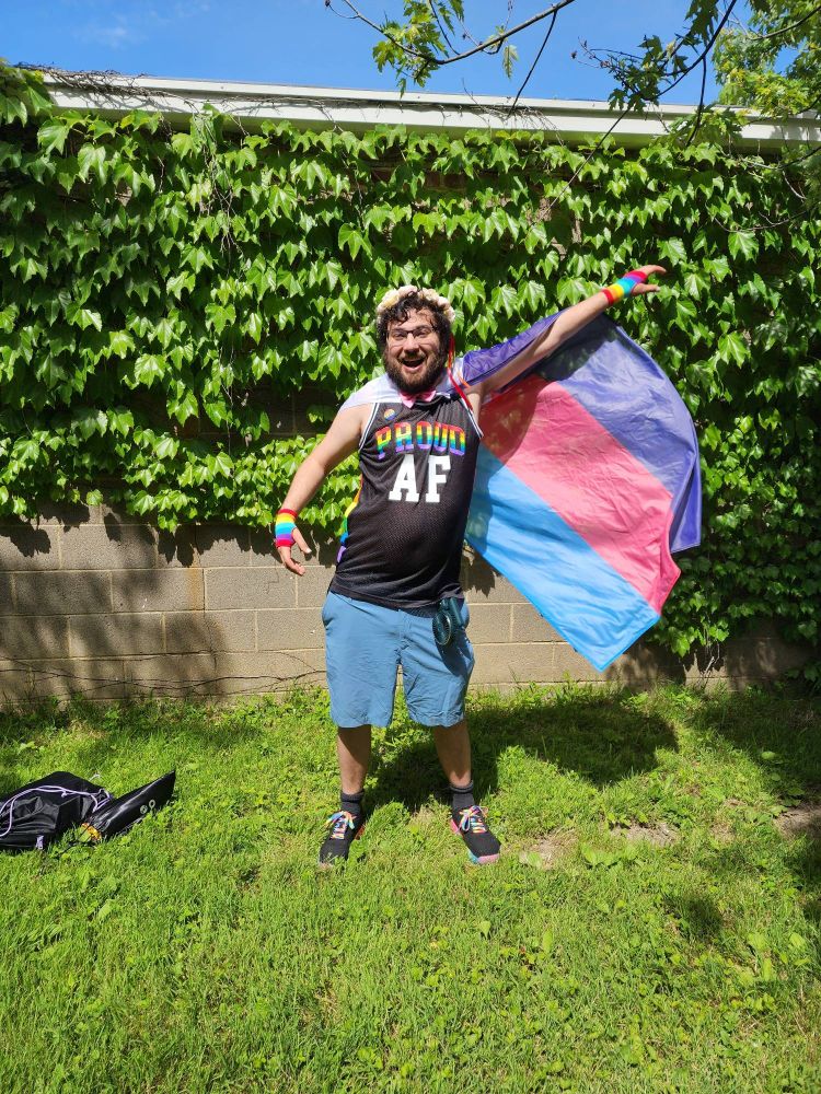 Person in a tank top that says "PROUD AF" swishing a polyamory flag cape
