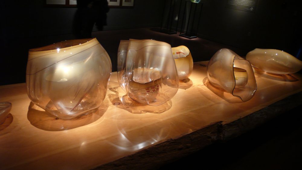 An exhibit of translucent champagne-colored glass bowls. The larger bowls have smaller bowls inside. Shadows surround the bowls, and light reflects off the bowls.