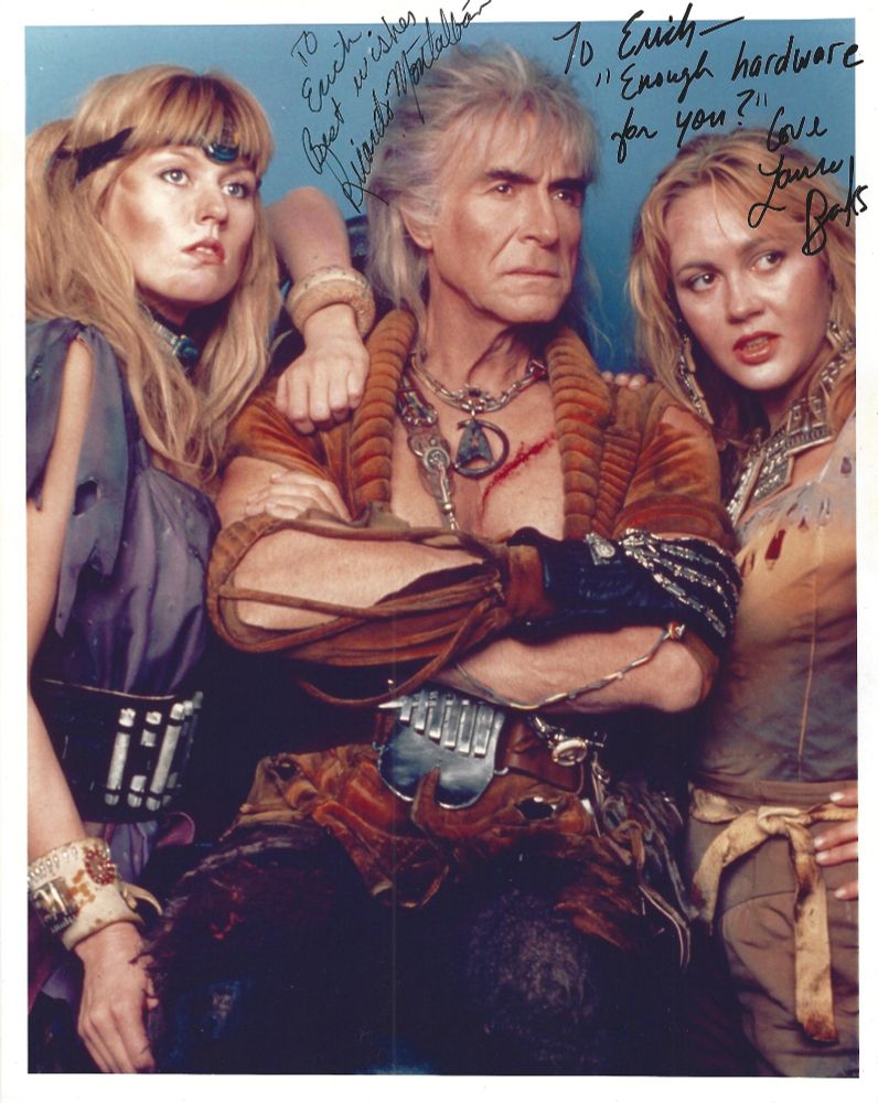 A color publicity photo from the movie "Star Trek: The Wrath of Khan," featuring Khan (Ricardo Montalban) flanked by two of his female crew members (played by Pam Bennett and Laura Banks). The photo is autographed by Ricardo Montalban (with the inscription reading "To Erich, Best wishes, Ricardo Montalban") and Laura Banks (with the inscription reading "To Erich -- 'Enough hardware for you?' Love, Laura Banks."