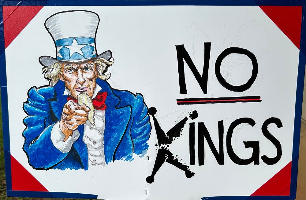 A drawing of Uncle Sam (originally by James Montgomery Flagg): An old white man with a long white chin beard and curly white hair; wearing a white top hat with a light blue hat band decorated with white stars, a dark blue top coat, and a red neck tie; pointing at the viewer with his right hand’s index finger. To the figure’s left are the words “no kings” in bold black letters, with the word “no” underscored. The letter K in the word “king” is a stylized broken crown, in support of No Kings Day.