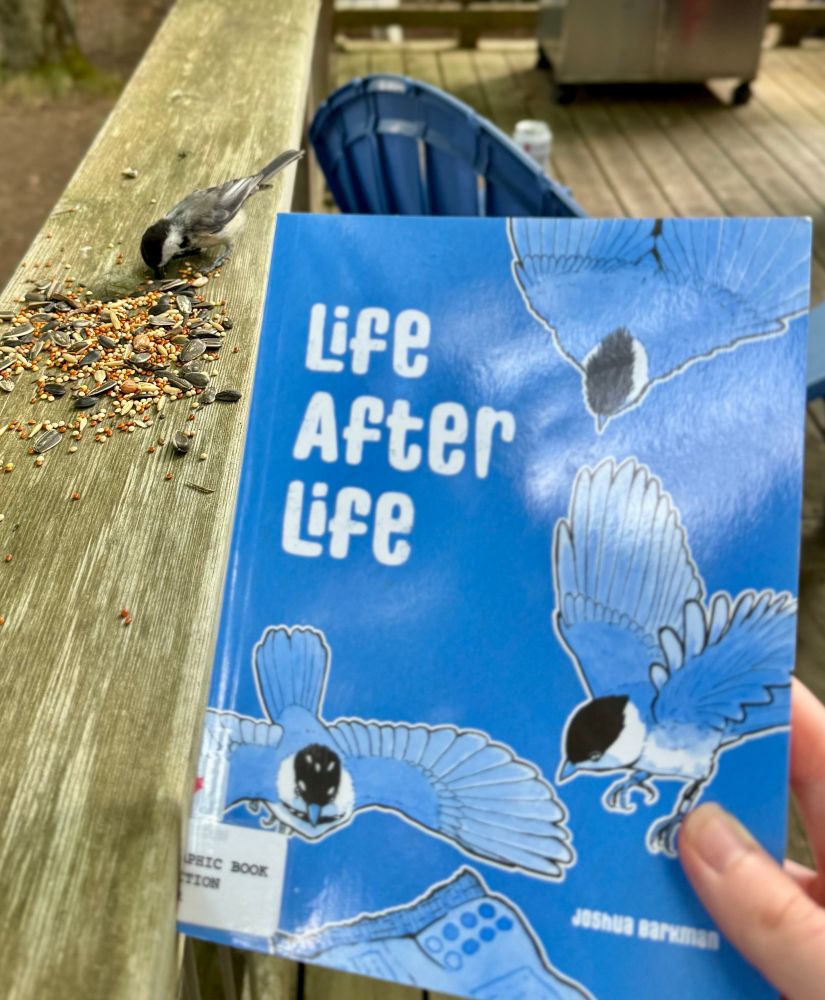 A chickadee eating seeds next to the book Life After Life by Joshua Barkman