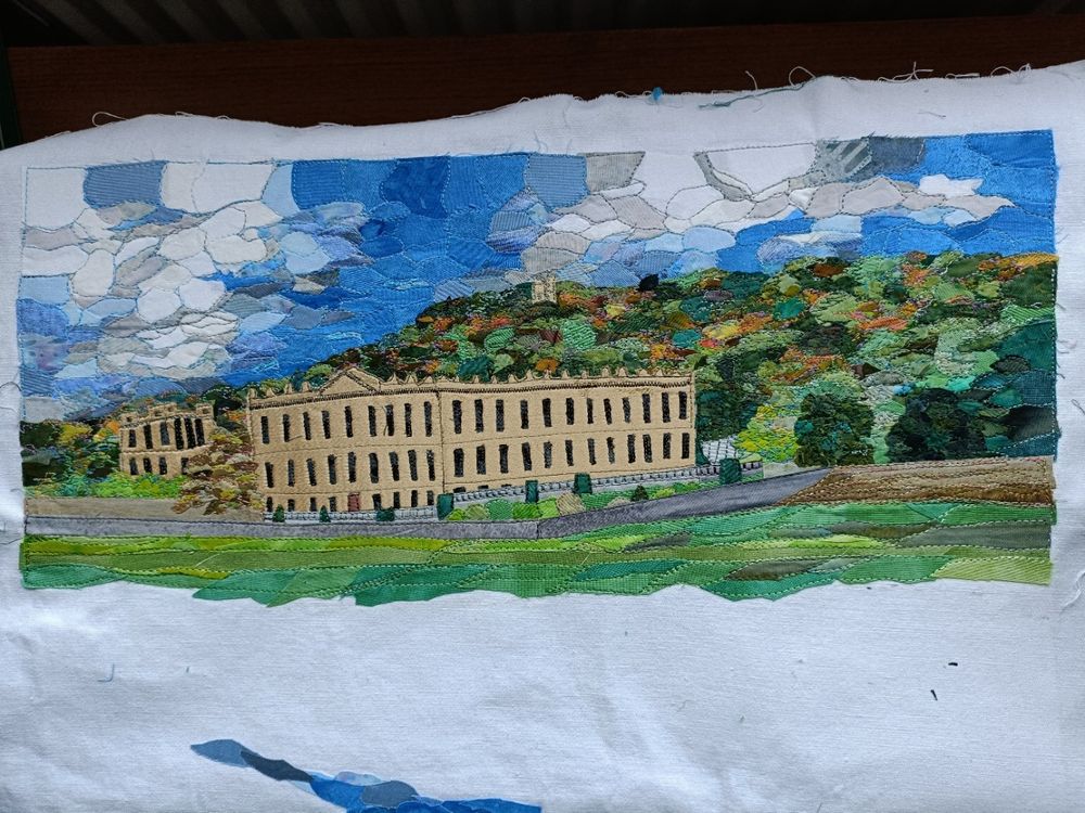 Partly completed textile picture of Chatsworth House with wooded hillside behind and grass in front, created from small pieces of fabric.