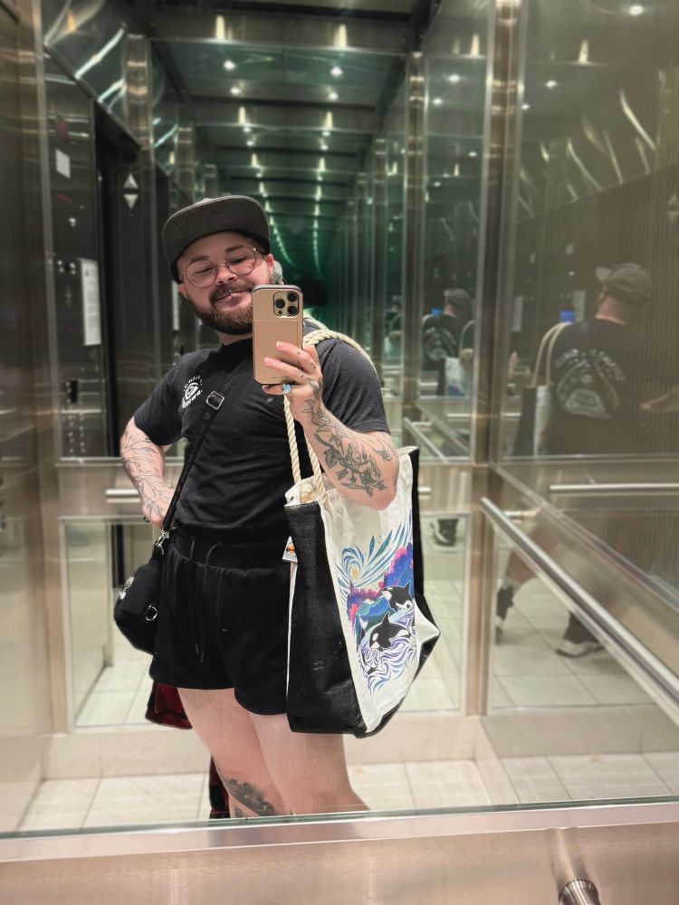 Selfie of myself, a queer transman wearing a cute, all black, summer fit featuring a shirt by Aware Wolf, mini bag by Death Petal and beach bag by Allosaurex / The Creature Collective