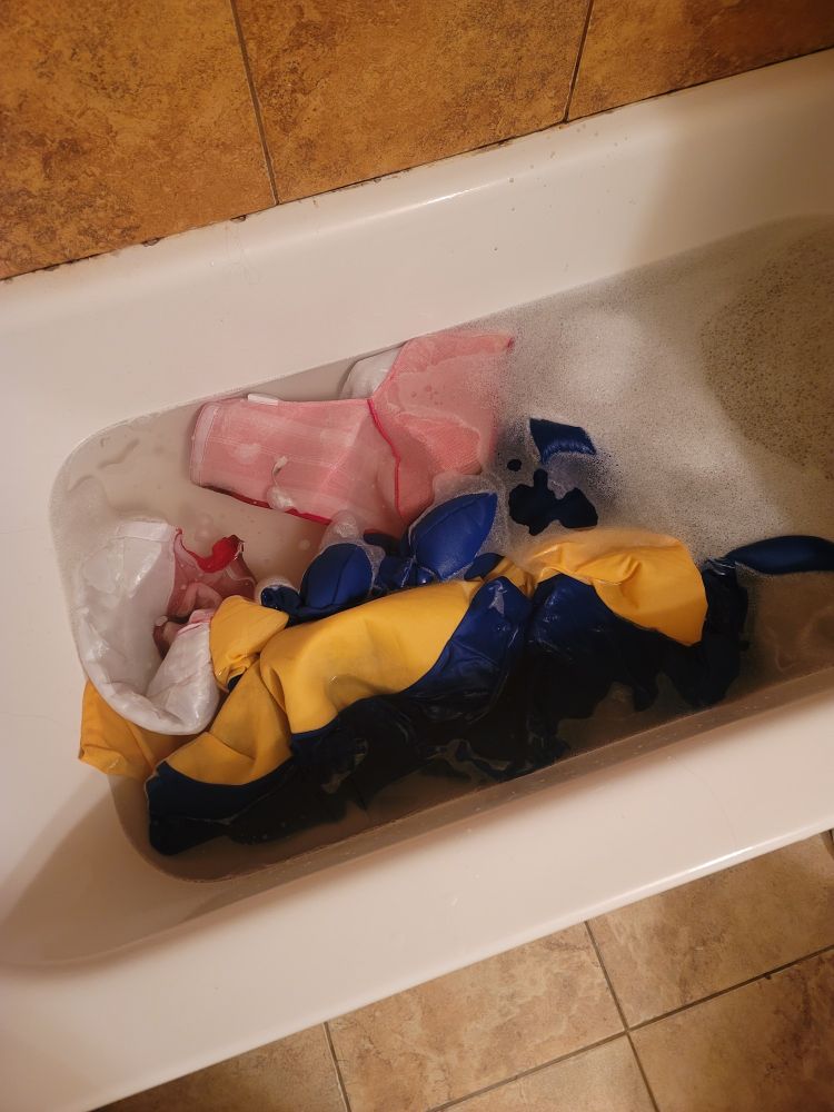 A photograph of a bathtub full of soapy water. In the soapy water are pieces of a Sonic the Hedgehog costume.