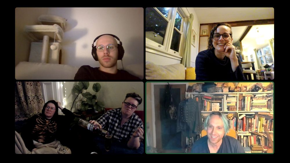 A screenshot of a video chat. The window is divided into four. A brooding young man with glasses, big headphones and a cat tree behind him. Penny, the best cat, is lounging with just the tip of her ear visible. Panel 2, a grinning woman with glasses and excellent wavy hair shaved on one side rests her chin on her hand in an intelligent looking pose. It is clear she took the screenshot because she looks best in it. It is light outside for her, because she is in Australia. In another panel two middle aged women with glasses short hair sit on battered leather couches under blankets in a dim room. One is wearing an excellent skeleton hoodie and gazing off into the middle distance. The other is pouring campari into an already full champagne flute. In the final panel, a smiling man with blue hair is dwarfed by his backdrop, which is a large, chaotic bookshelf disappearing off the frame into the distance. Atop  it are all manner of objects from funkopops to tophats, and on the bookshelves hangs a button covered military jacket that no longer fits him. He is the only person not wearing glasses. 
