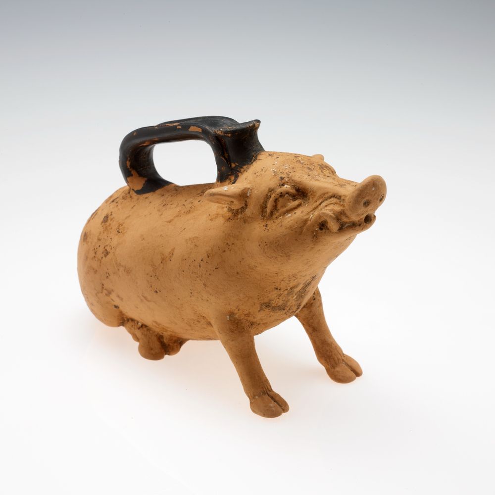 A small terracotta pitcher, originally used for oil, in the shape of a wild boar. He is curling is lips up over his tusks like he is trying to look mean, but his ears are back and his little rear trotters are tucked up under him like he’s shy, so the effect is funny and adorable. 