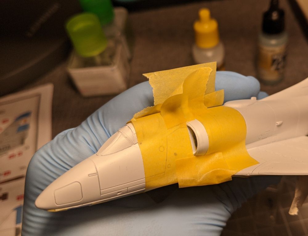 An airplane model is partially covered in yellow masking tape, leaving a little bit of the intake exposed.