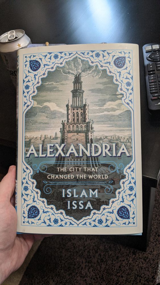 A beautiful hand holds a book. The title is 'Alexandria: The city that changed the world' by Islam Issa.