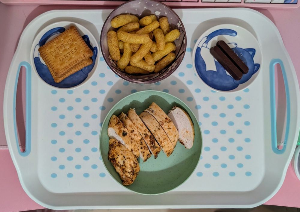 A tray containing little plates with: 
A cooked chicken breast
A packet of marmite cheese puffs
3 Petit Lu salt crackers
2 Hotel Chocolat batons