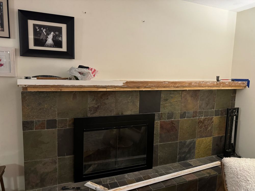 A tiled fireplace. The mantel has been partially stripped of white paint and dismantled, revealing a dark hardwood on top of a pine base. It is not clear from the picture (nor in the photographer’s mind) what the end result will be