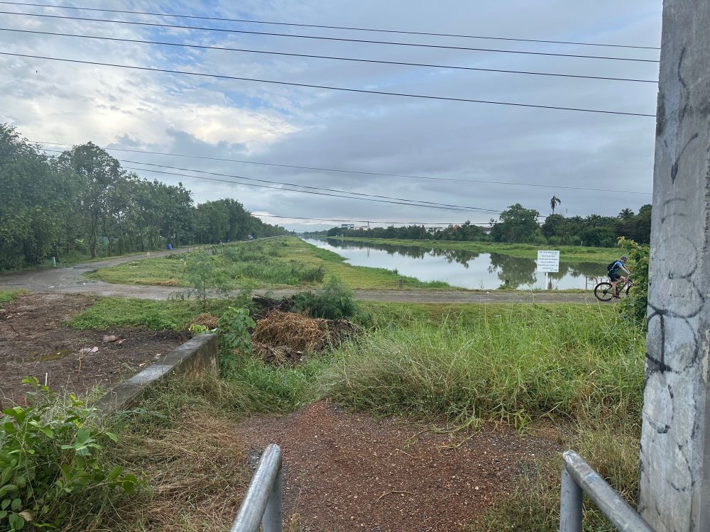 A large canal in bangkok, with a wide gravel path on the left side.