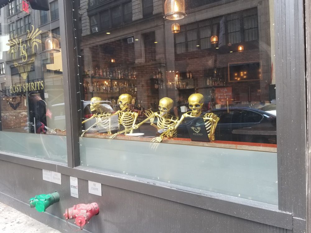 A bar window showing 4 gold skeletons drinking at a counter. One is reading a menu.