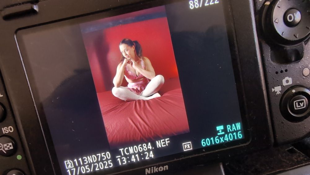 Model Alora Lux sitting on a bed, legs crossed with a cheeky look on her face, wearing a small and revealing DDLG style outfit 