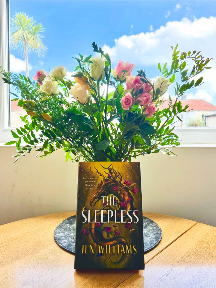 A copy of The Sleepless, propped against a bouquet of pink and white roses 