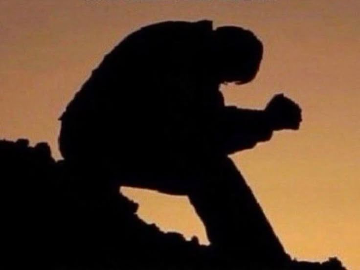 silhouette of a figure sitting down and leaning over with their hands grasped together