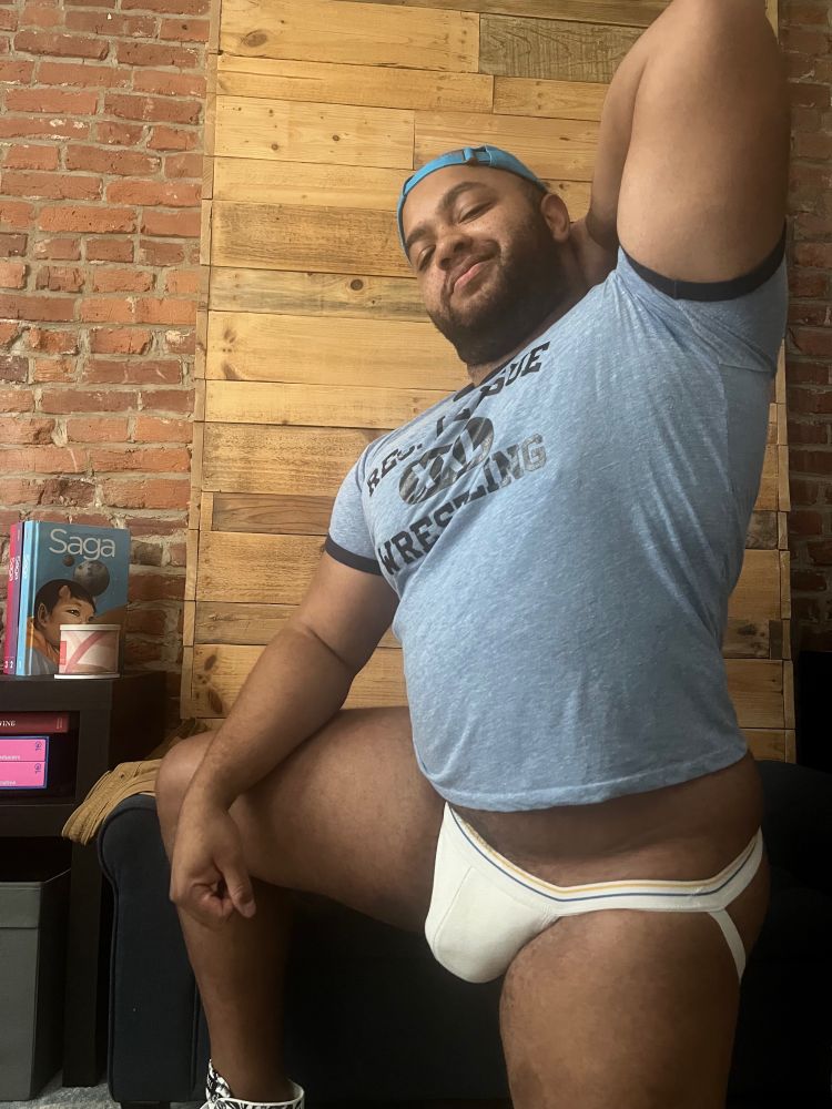 Portrait of a gay man kneeling wearing a blue wrestling tee and a white jock 