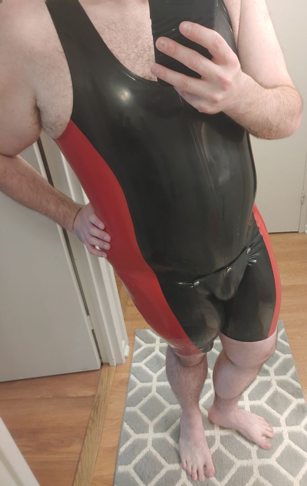 Posing in a rubber singlet, it's black with a solid red stripe from the outside of the leg to armpit. It also has a black codpiece.