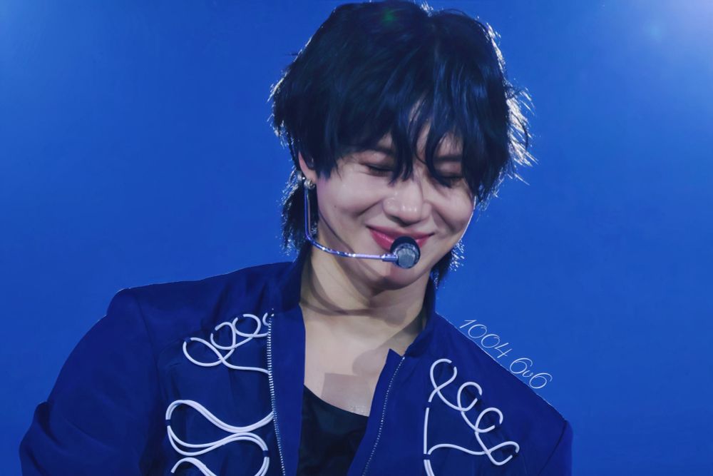 Taemin onstage looking down and smiling with fluffy dark hair in a blue suit with white details