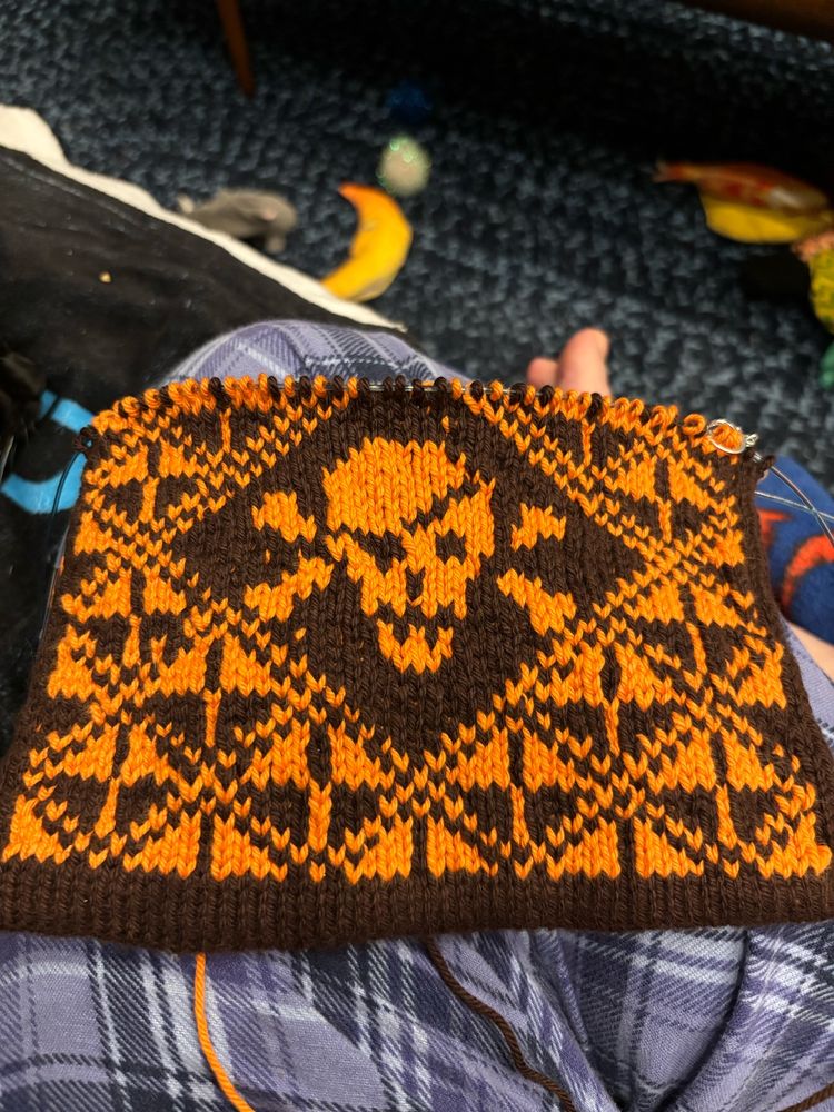 A black and orange knitted potholder with a skull and crossbones design.