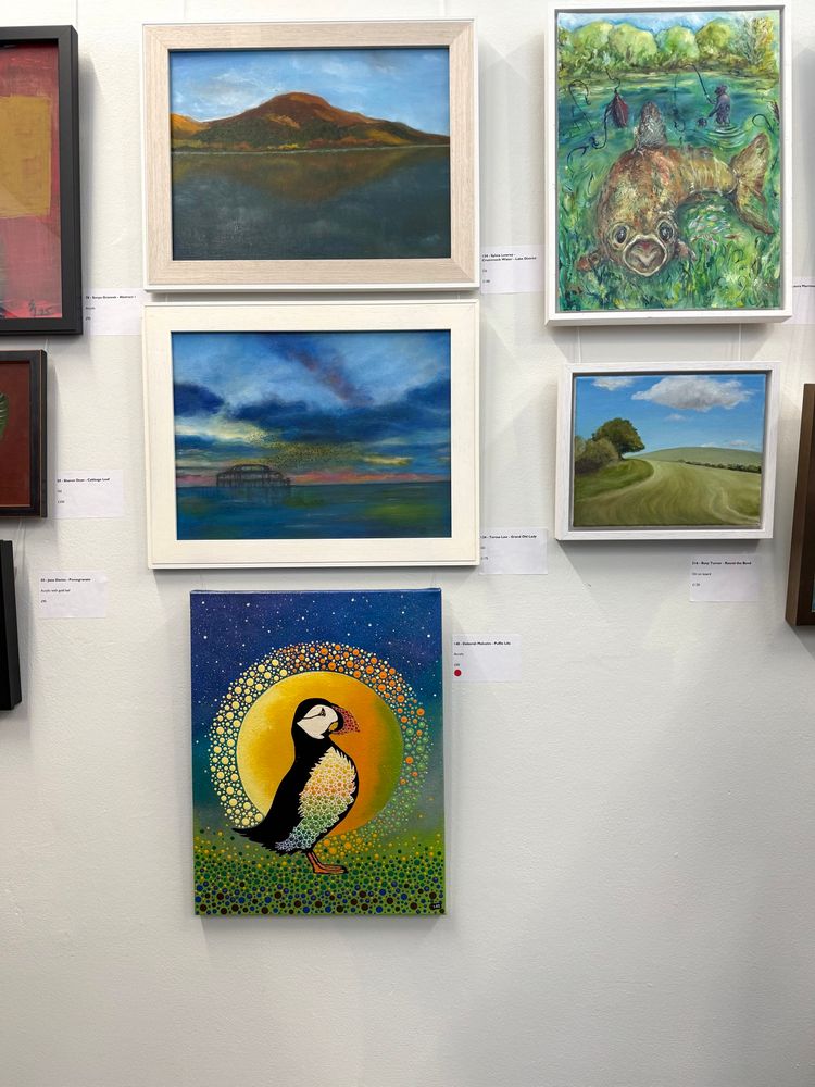 5 paintings hanging in a gallery. The top four are muted landscapes. The bottom one is a bright painting of a Puffin. 