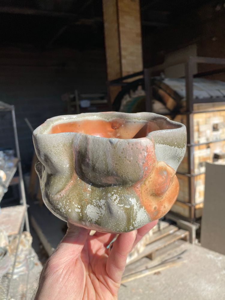 A wood-fired ceramic bowl with glazes and undulating contours, held in hand.