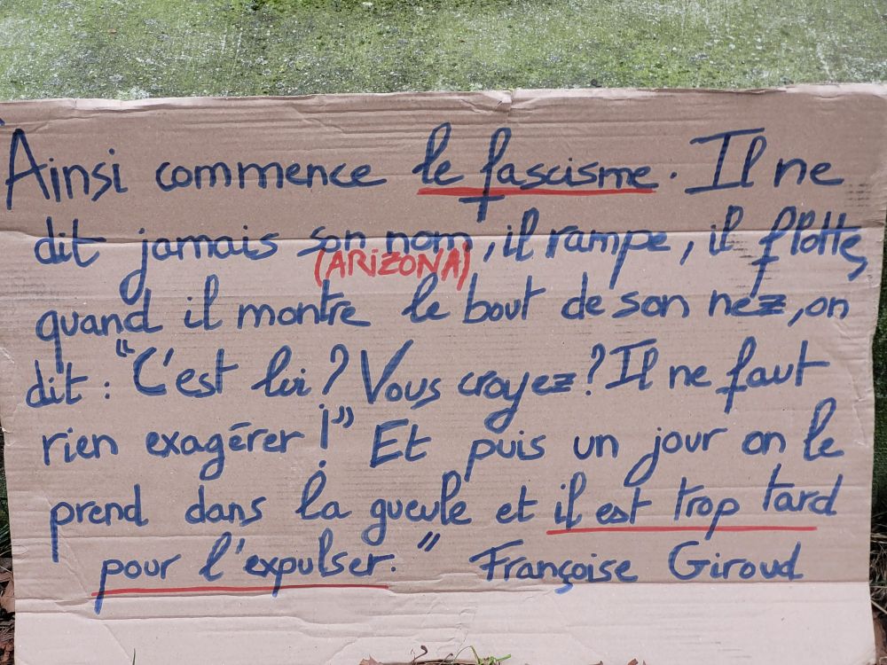 Photo d'une pancarte en carton sur laquelle est écrit en bleu " Ainsi commence le fascisme. Il ne dit jamais son nom (Arizona), il rampe, il flotte, quand il montre le jour de son nez, on dit <<C'est lui ? Vous croyez ? Il ne faut rien exagéré !>>. Et puis un jour on le prend dans la gueule et il est trop tard pour l'expulser. Françoise Giroud"
Les mots "fascisme" et "il est trop tard pour l'expulser" sont soulignés en rouge. Le mot "Arizona" est écrit en rouge. 