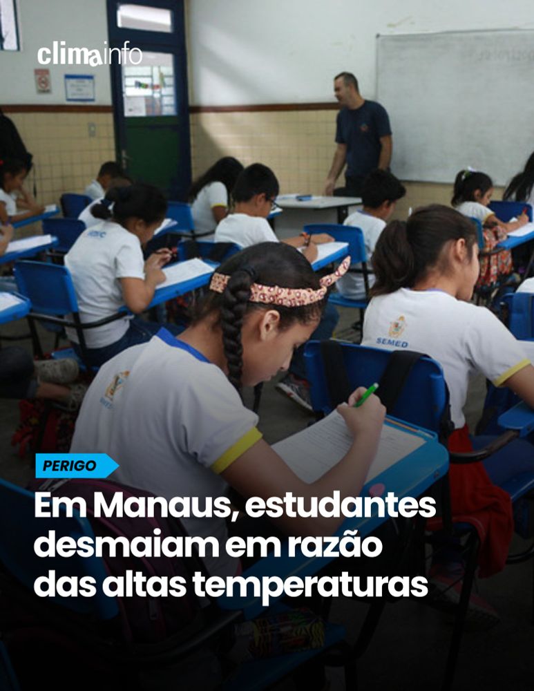 sala de aula com alunos sentados em suas carteiras escrevendo em um papel. Ao fundo, o professor está em pé ao lado da lousa. 