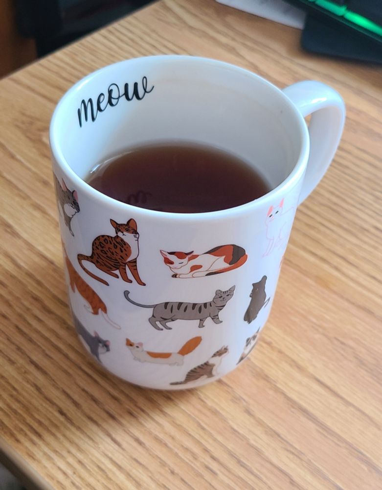 A white mug with little cats on the outside. "Meow" is written on the inside.