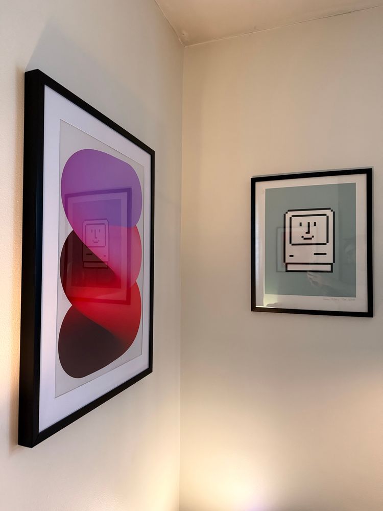 A photo of a wall with a print by Jerry-Lee Bosmans and a print by Susan Kare, Happy Mac. 