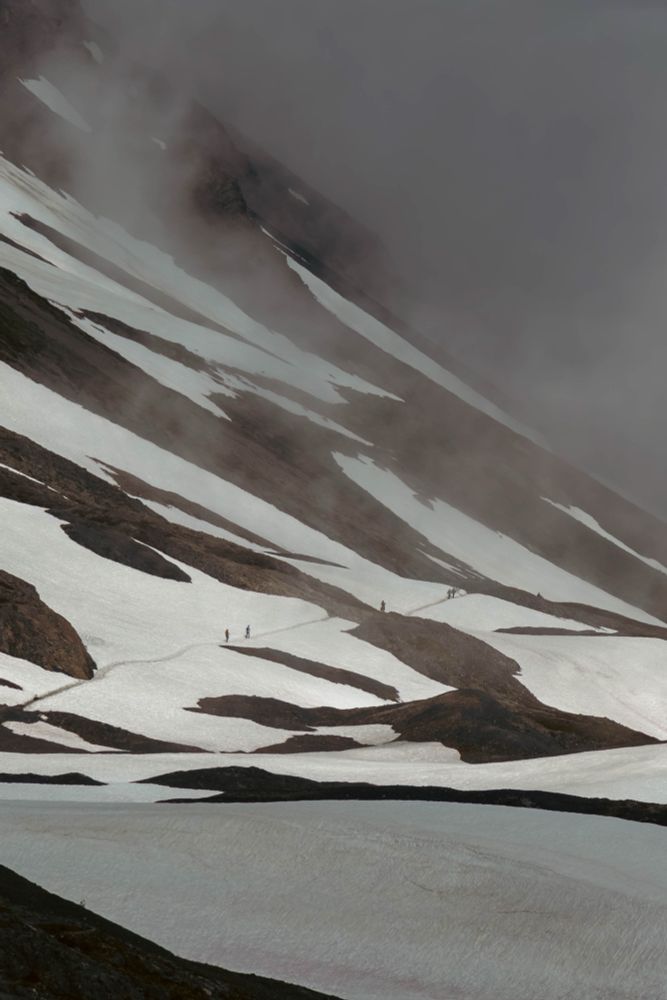 A group of people on a trail in the snow walk towards mist