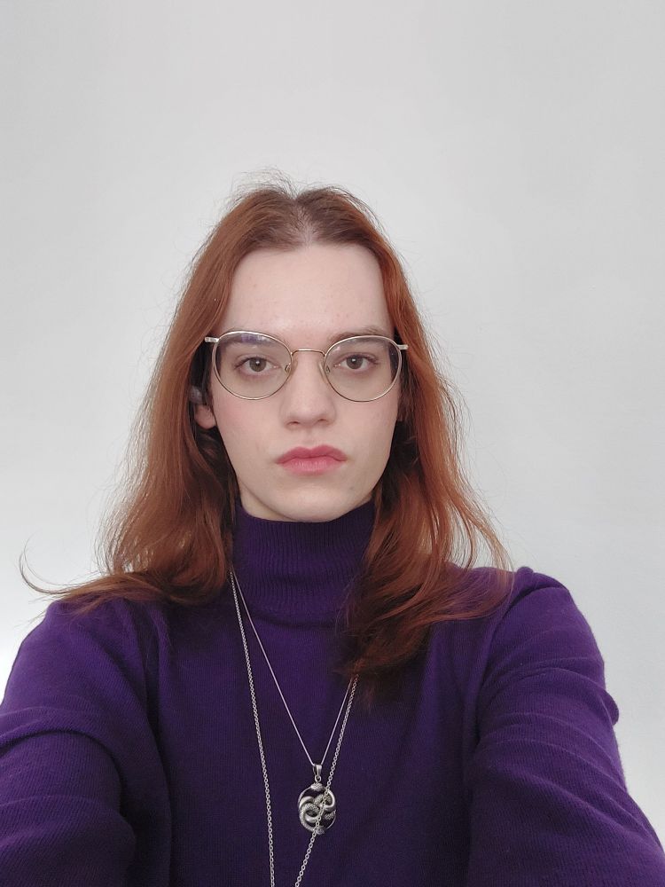 Selfie of me im front of a white wall, wearing a purple turtleneck.