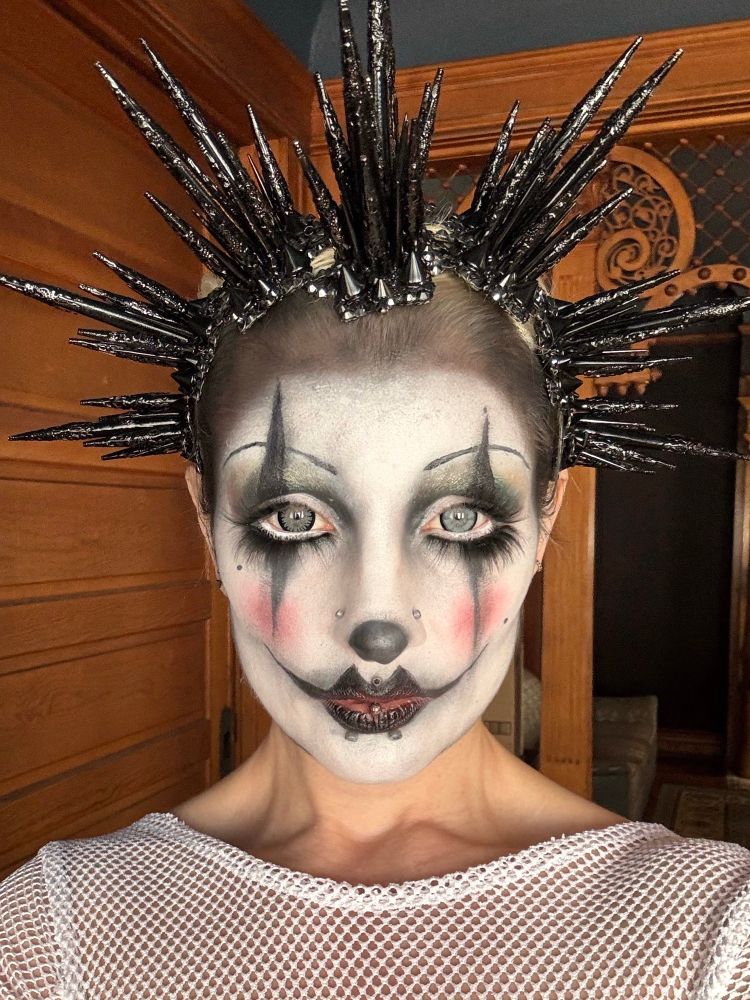 Selfie shot face on of model Ulorin Vex in heavy creative gothic clown/harlequinn makeup and wearing a spikey black crown. The backdrop is the interior of a victorian house with all original wood features