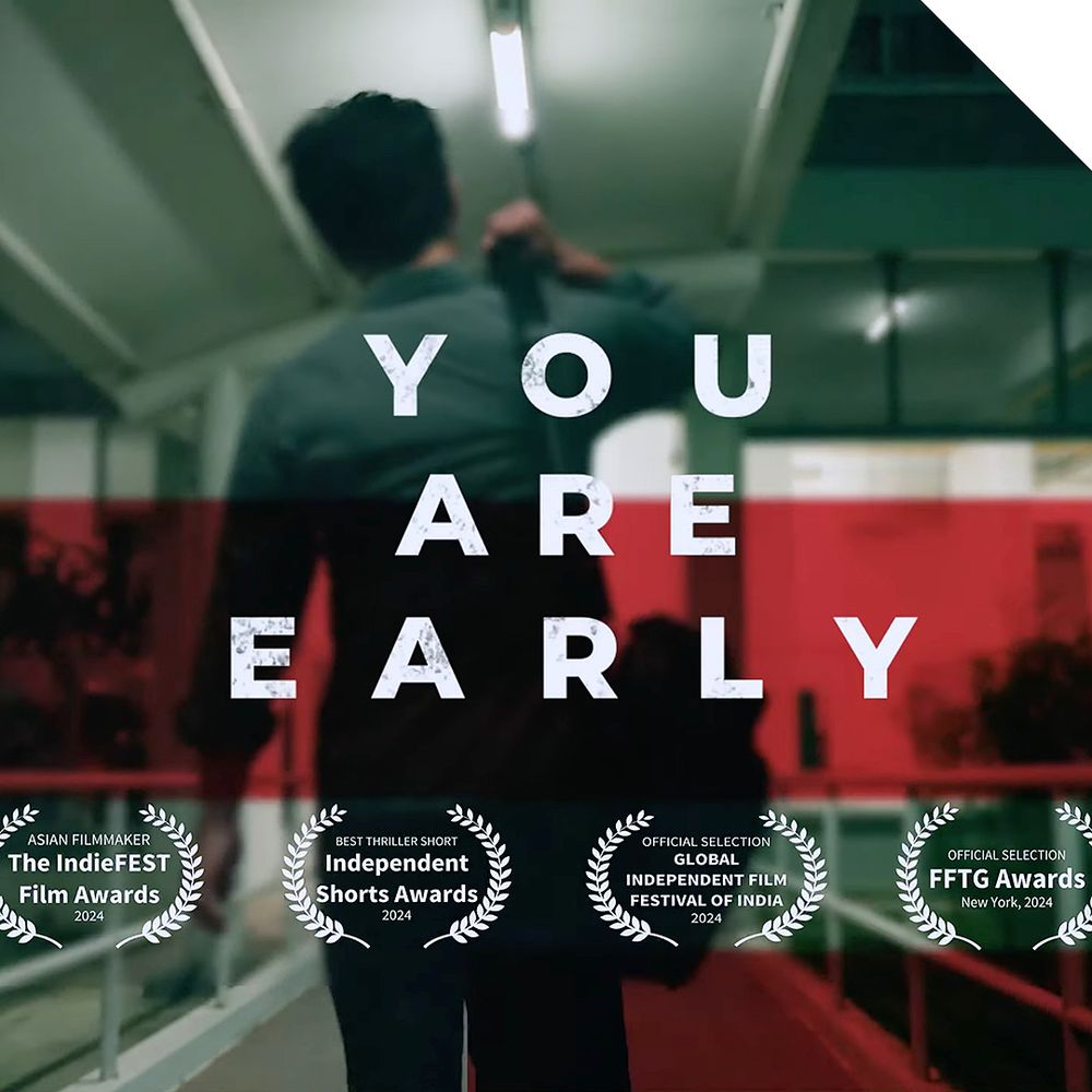 frame from the trailer for Ashish Sharma’s production of *You’re Early* – it shows a modern, cool-coloured interior with a male figure walking away while he adjusts the strap of his shoulder bag 

overlayed on the image is the title: YOU ARE EARLY 
below this are four laurel wreath graphics containing the following text:
• Asian Filmmaker – the IndieFEST Film Awards – 2024
• Best Thriller Short – Independent Shorts Awards – 2024
• Official Selection – Global Independent Film Festival of India – 2024
• Official Selection – FFTG Awards – New York, 2024