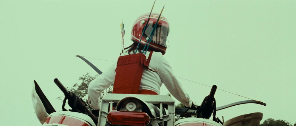 Cleopatra on a motorbike with rear-facing machine guns mounted to the saddlebags