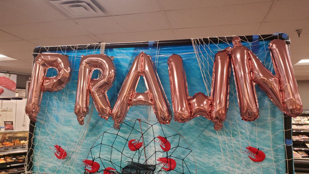 Pink balloon letters in a grocery store display that simply say PRAWN