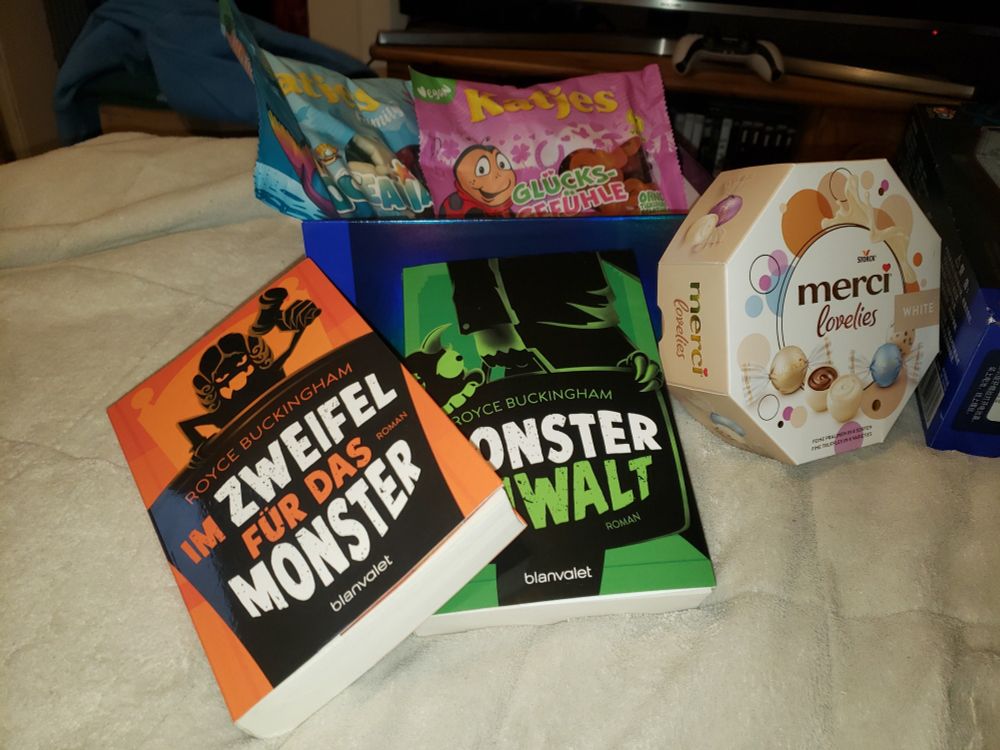 Ein geöffnetes Päckchen, mit verschiedenen Katjes Weingummis einer Packung Merci Lovelies White sowie 2 Büchern von Royce Buckingham "Im Zweifel für das Monster" und "Monster Anwalt"