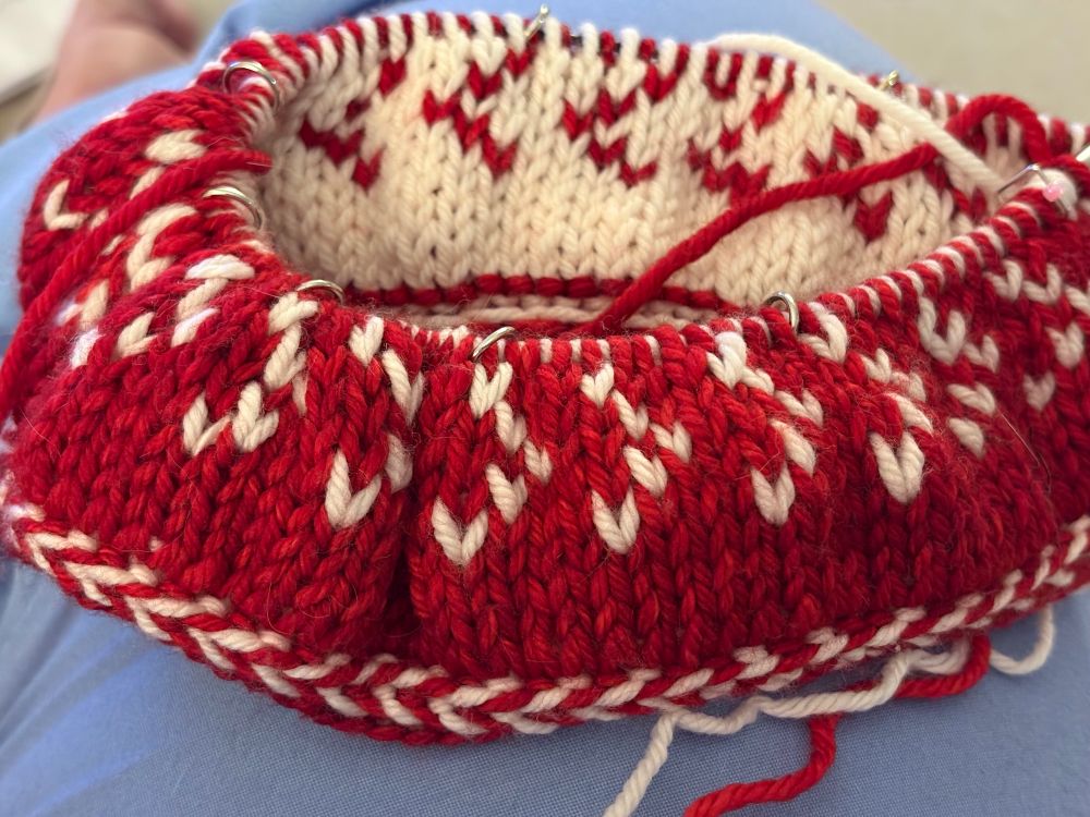 Picture shows a knitting project in red and white yarn. It is a double-layered hat in progress. 